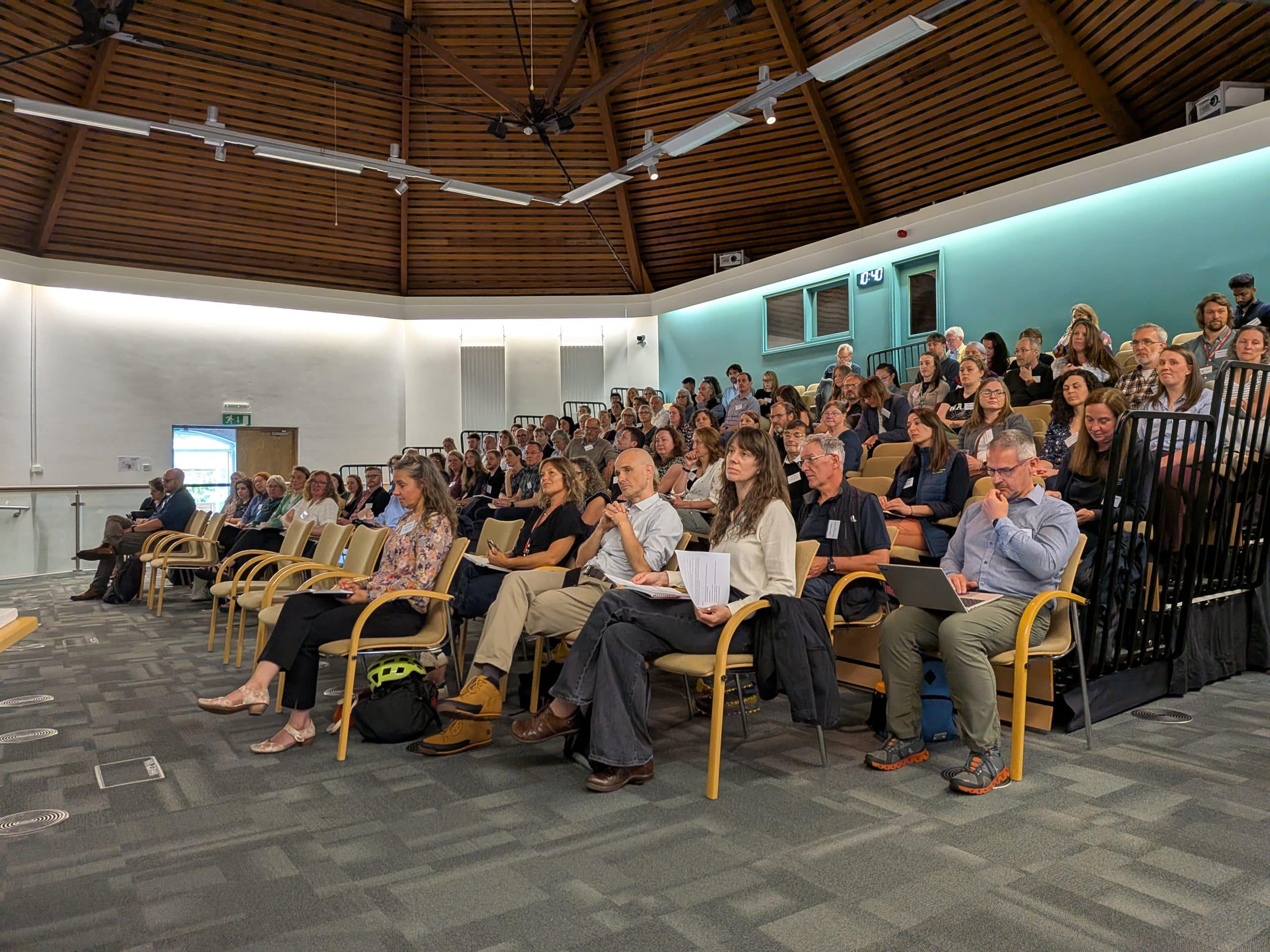 Auditorium with 100 people sat in seats looking at something out of frame